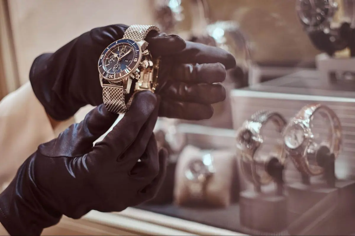 A pair of hands in black gloves holding a luxury watch